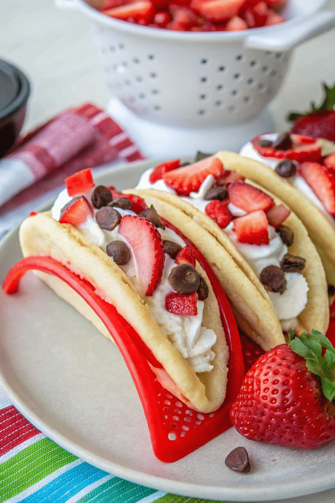 Pancakes stuffed with creamy cheesecake mousse, fresh strawberries, and chocolate chips, served in a vibrant red taco holder.