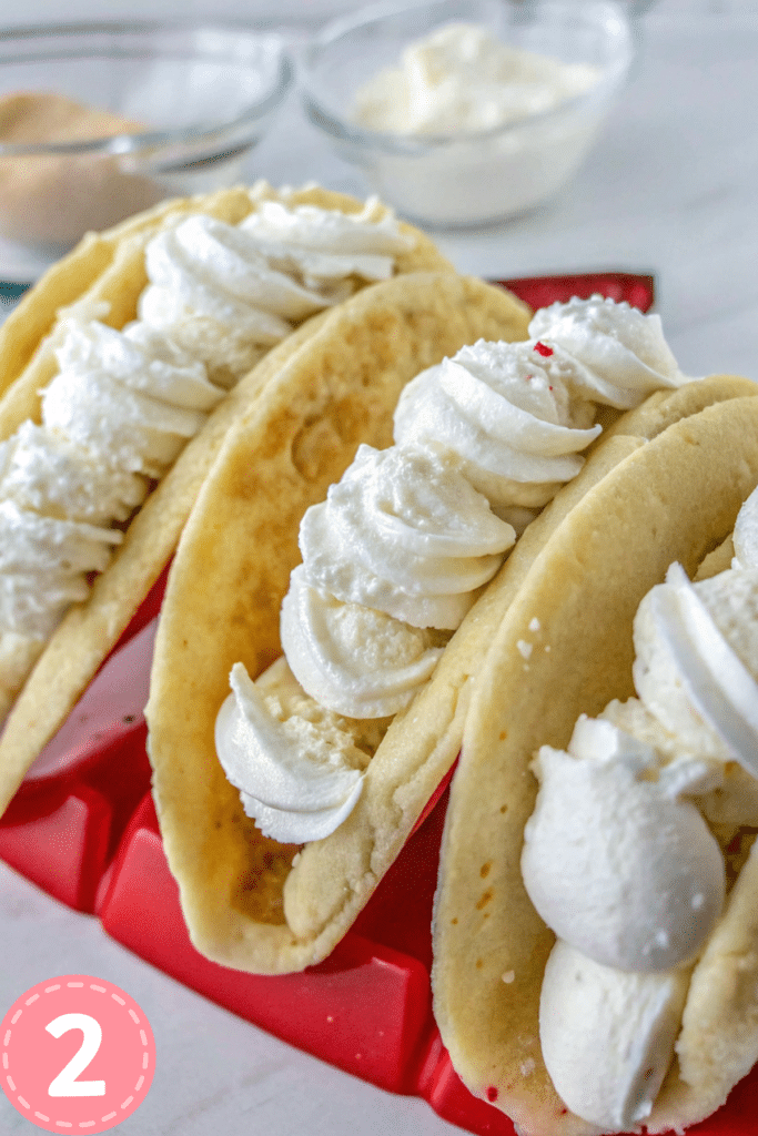 Cheesecake mousse-filled pancakes topped with strawberries and chocolate chips in a red taco holder